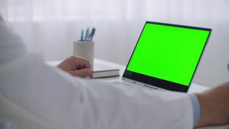 doctor-is-listening-patient-at-online-consultation-by-video-call-and-writing-notes-laptop-with-green-screen-for-chroma-key-technology